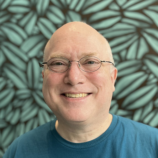 Mugshot of Glenn Fleishman wearing glasses showing pattern leaves in the background, by Lynn D. Warner